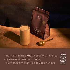 Glass of protein shake next to a bag of Brave Ancestral Protein on a wooden surface with a dark background.