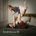 Woman lying on a bed with a child playfully lifting her leg, with text 'For all that you lift' on a neutral background.