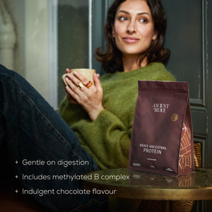 Woman holding a mug with a package of Brave Ancestral Protein on a table.