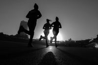 Three runners in silhouette against a dark background with a bright light source.